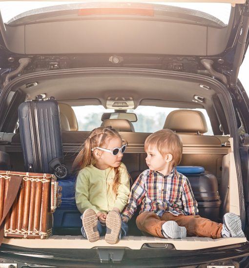 No road is long with good company. Little cute kids in the trunk of a car with suitcases looking at
