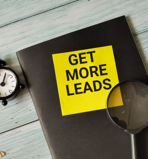 Phrase get more leads written on sticky note with alarm clock,magnifying glass and book.