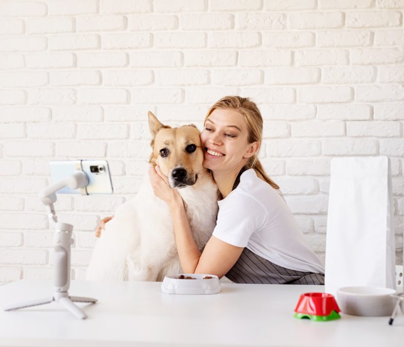 Young caucasian woman groomer blogger speaking looking to camera, having stream with her dog